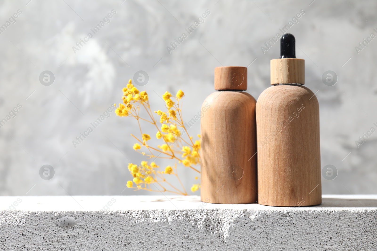 Photo of Bottles of cosmetic products and yellow gypsophila flowers on concrete surface against gray background, space for text