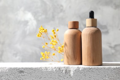 Bottles of cosmetic products and yellow gypsophila flowers on concrete surface against gray background, space for text