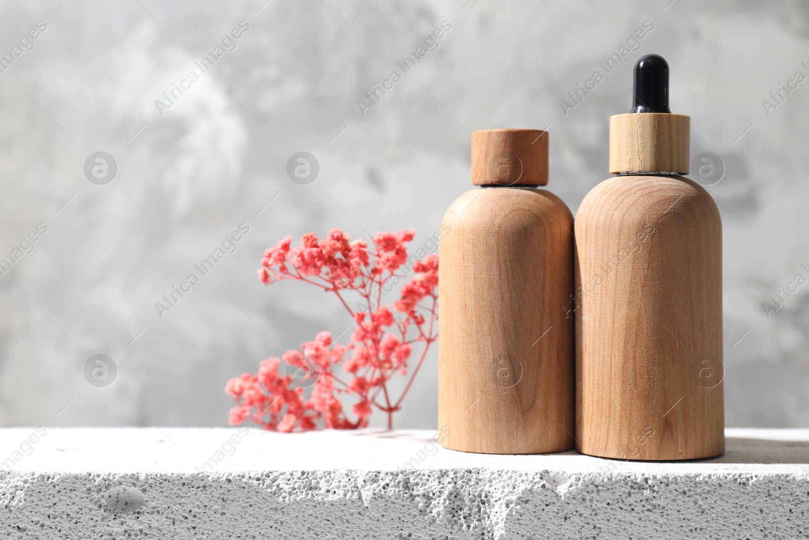 Photo of Bottles of cosmetic products and pink gypsophila flowers on concrete surface against gray background, space for text