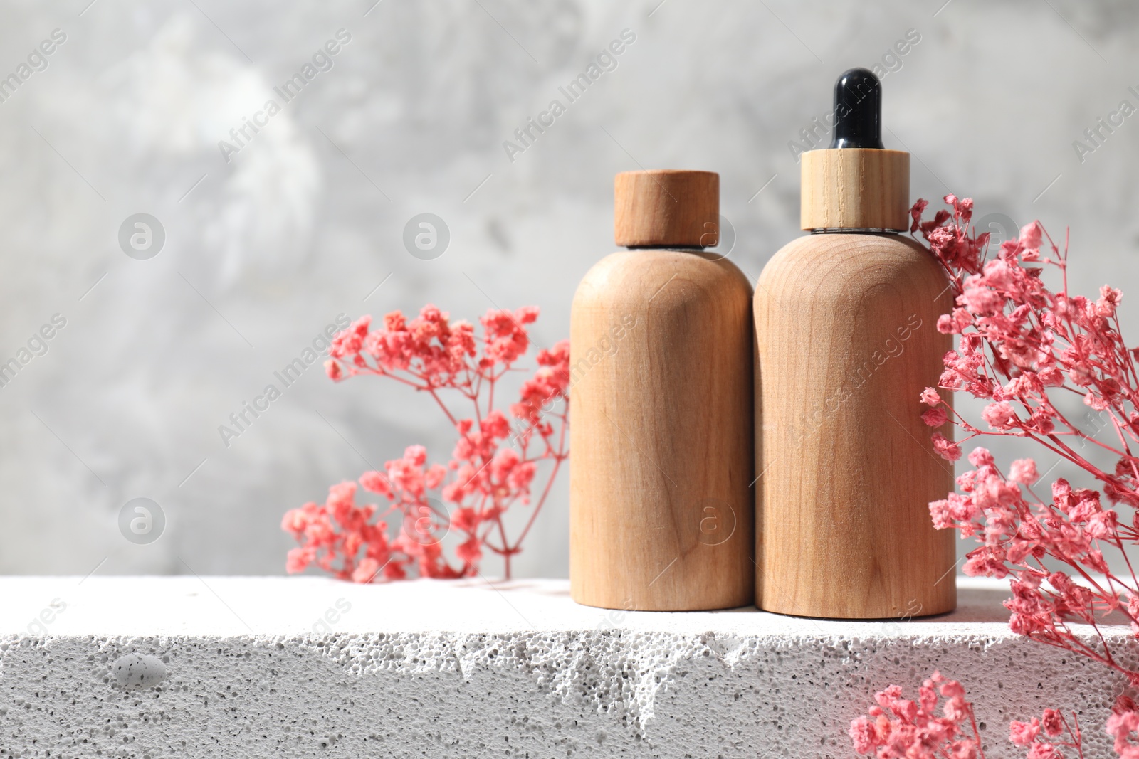 Photo of Bottles of cosmetic products and pink gypsophila flowers on concrete surface against gray background, space for text