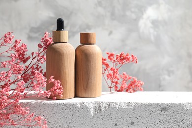 Bottles of cosmetic products and pink gypsophila flowers on concrete surface against gray background, space for text