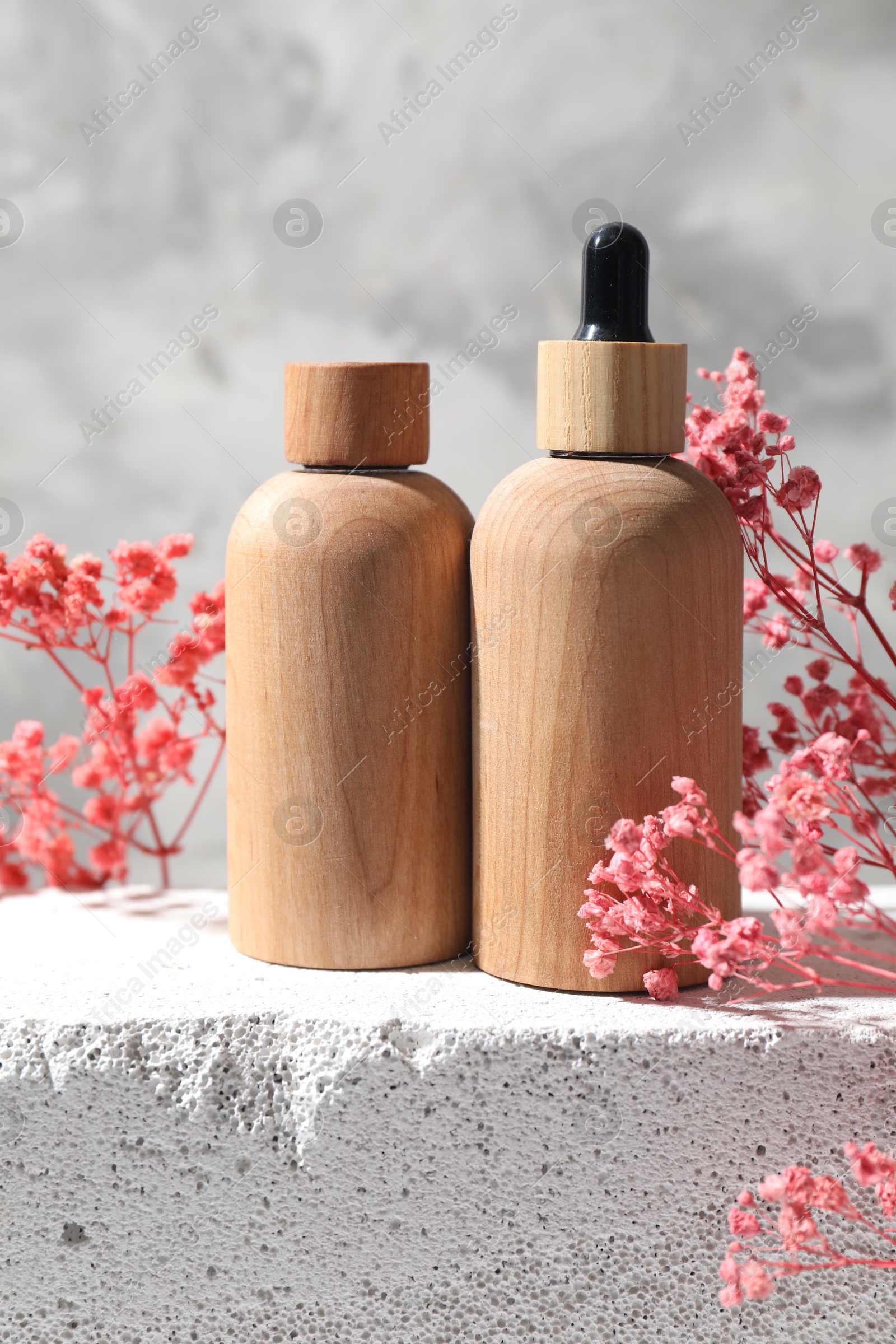 Photo of Bottles of cosmetic products and pink gypsophila flowers on concrete surface against gray background