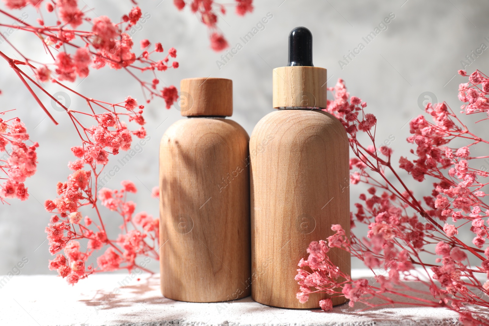 Photo of Bottles of cosmetic products and pink gypsophila flowers on concrete surface against gray background