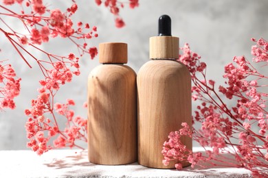 Bottles of cosmetic products and pink gypsophila flowers on concrete surface against gray background