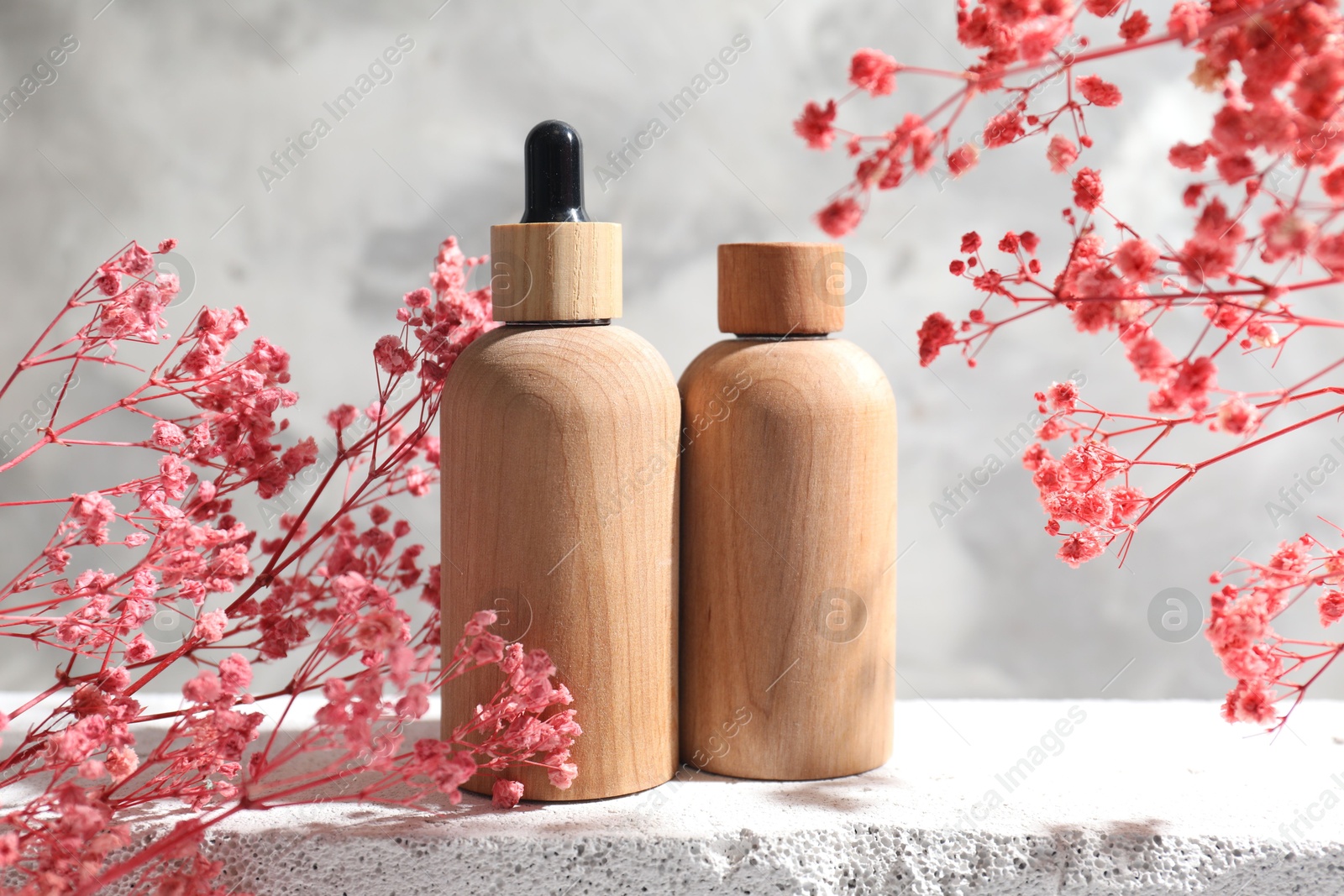 Photo of Bottles of cosmetic products and pink gypsophila flowers on concrete surface against gray background