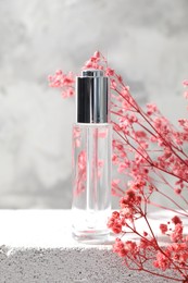 Photo of Bottle of serum and pink gypsophila flowers on concrete surface against gray background