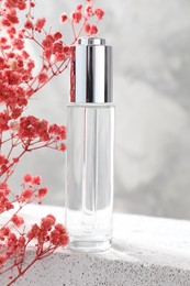 Bottle of serum and pink gypsophila flowers on concrete surface against gray background