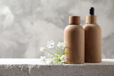 Bottles of cosmetic products and beautiful white flowers on concrete surface against gray background, space for text