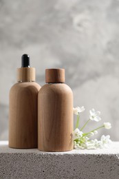 Bottles of cosmetic products and beautiful white flowers on concrete surface against gray background