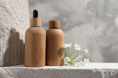 Bottles of cosmetic products and beautiful white flowers on concrete surface against gray background, space for text