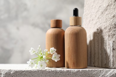 Bottles of cosmetic products and beautiful white flowers on concrete surface against gray background