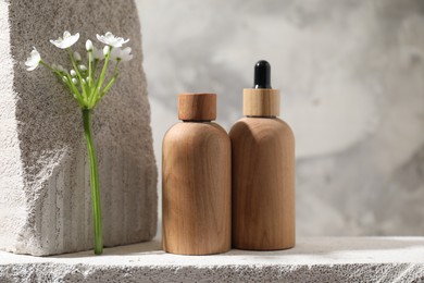 Bottles of cosmetic products and beautiful white flowers on concrete surface against gray background