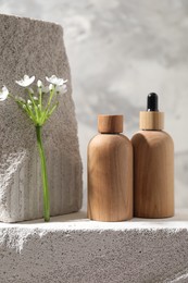 Bottles of cosmetic products and beautiful white flowers on concrete surface against gray background