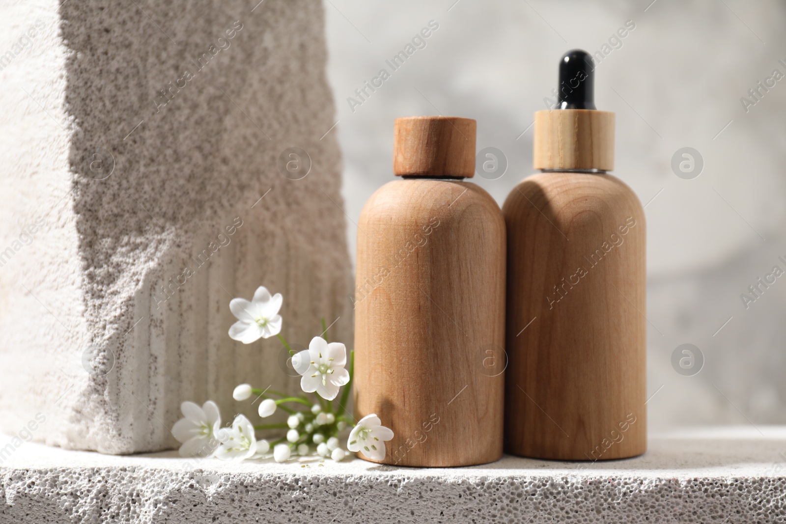 Photo of Bottles of cosmetic products and beautiful white flowers on concrete surface against gray background