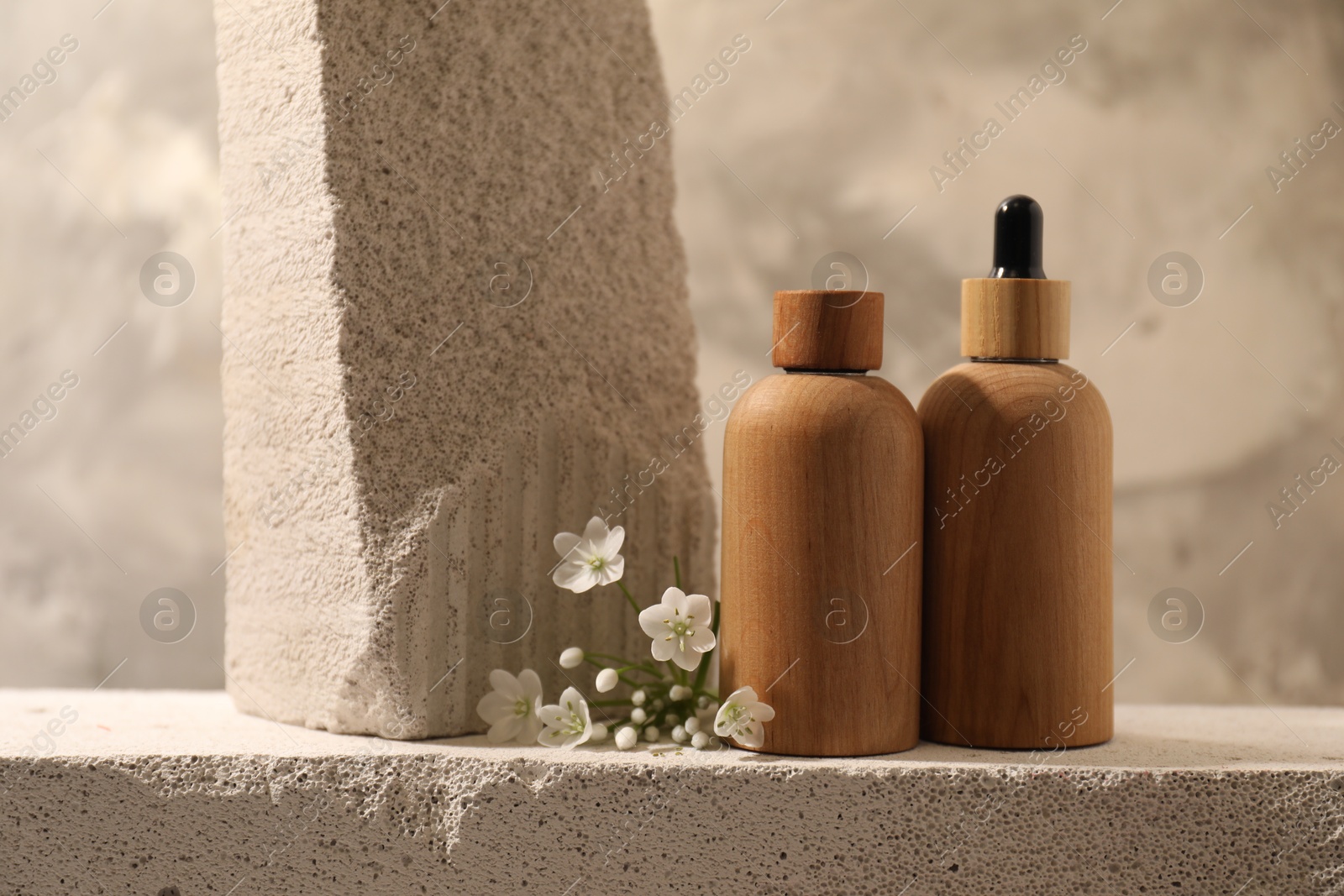 Photo of Bottles of cosmetic products and beautiful white flowers on concrete surface against gray background, space for text