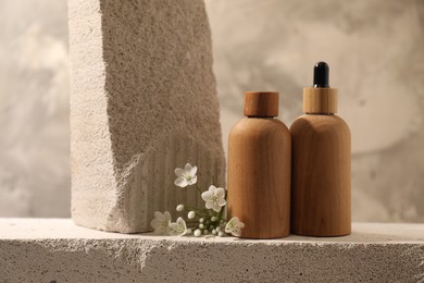 Bottles of cosmetic products and beautiful white flowers on concrete surface against gray background, space for text