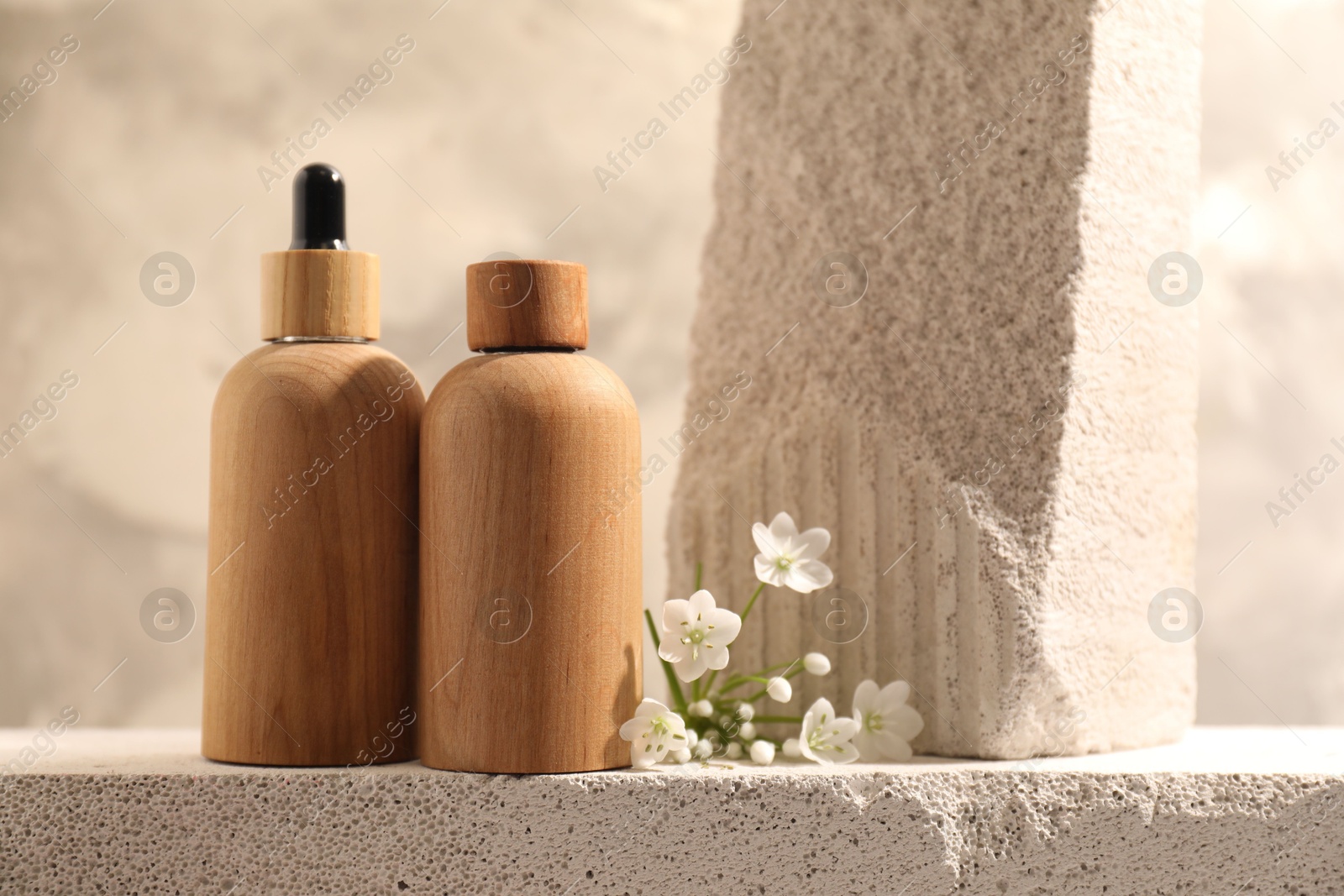 Photo of Bottles of cosmetic products and beautiful white flowers on concrete surface against gray background, space for text