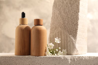 Bottles of cosmetic products and beautiful white flowers on concrete surface against gray background, space for text