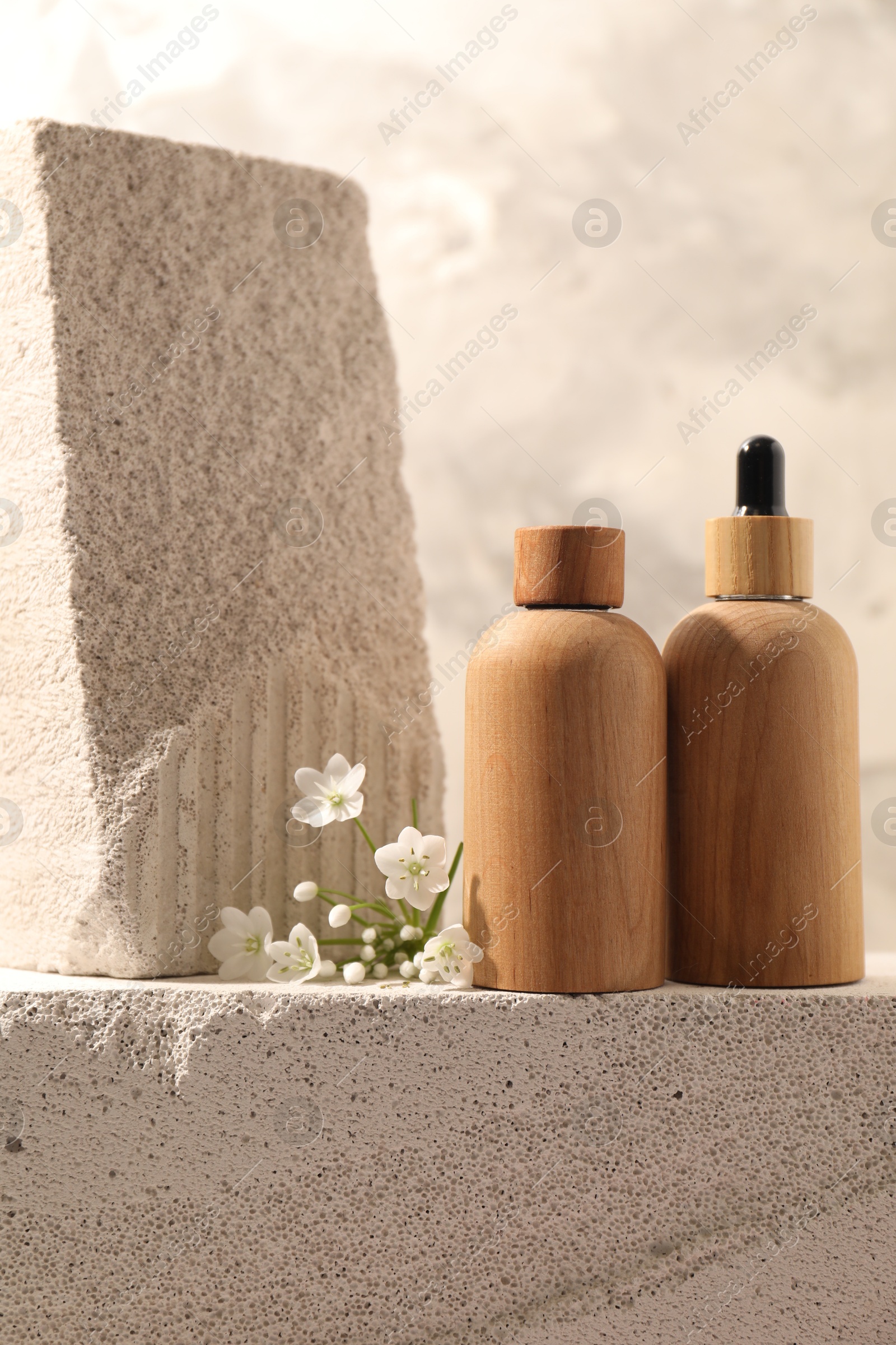 Photo of Bottles of cosmetic products and beautiful white flowers on concrete surface against gray background