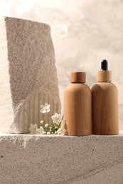 Photo of Bottles of cosmetic products and beautiful white flowers on concrete surface against gray background