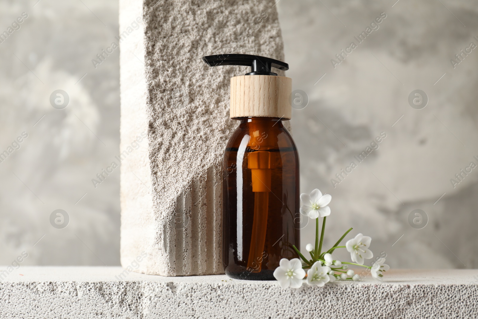 Photo of Bottle of cosmetic product and beautiful white flowers on concrete surface against gray background