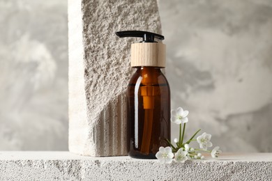 Bottle of cosmetic product and beautiful white flowers on concrete surface against gray background