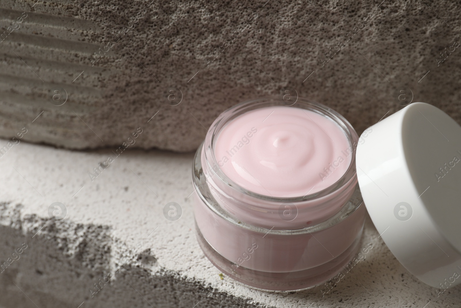 Photo of Jar of cream and lid on concrete block, space for text