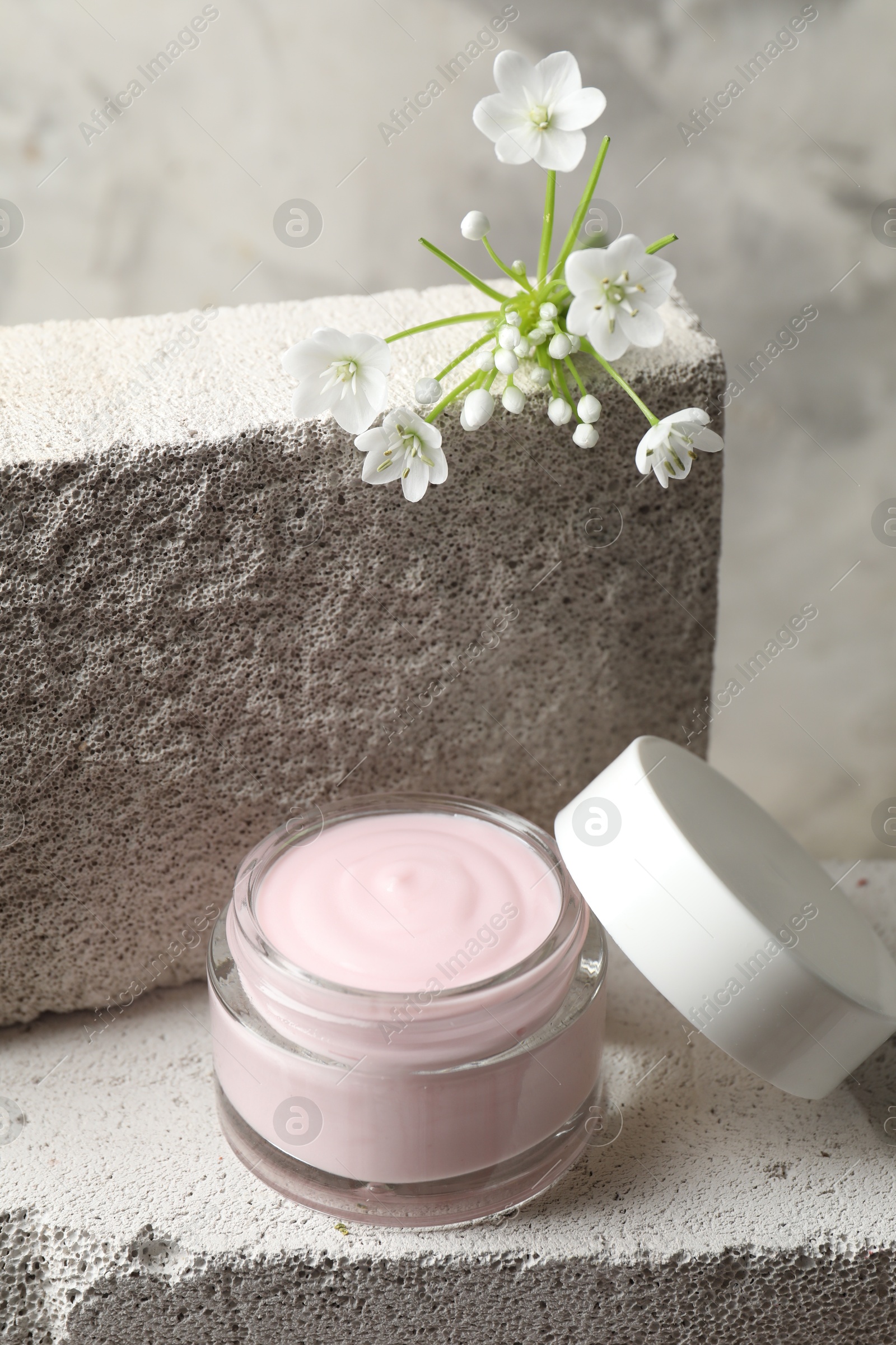 Photo of Jar of cream and beautiful white flowers on concrete blocks