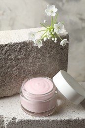 Jar of cream and beautiful white flowers on concrete blocks