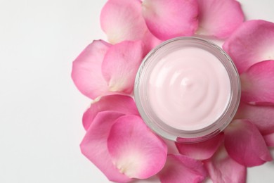 Photo of Jar of cream and pink petals on white background, top view. Space for text