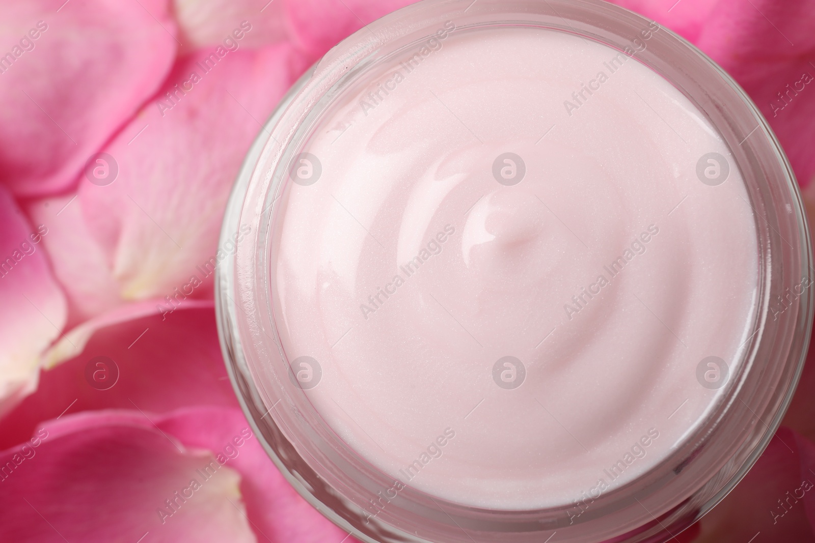 Photo of Jar of cream on pink petals, top view