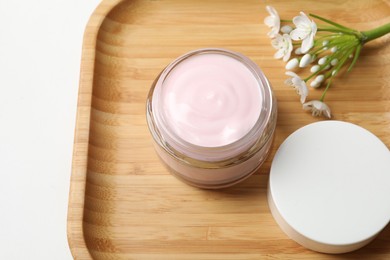 Photo of Jar of cream and beautiful flowers on white table, above view