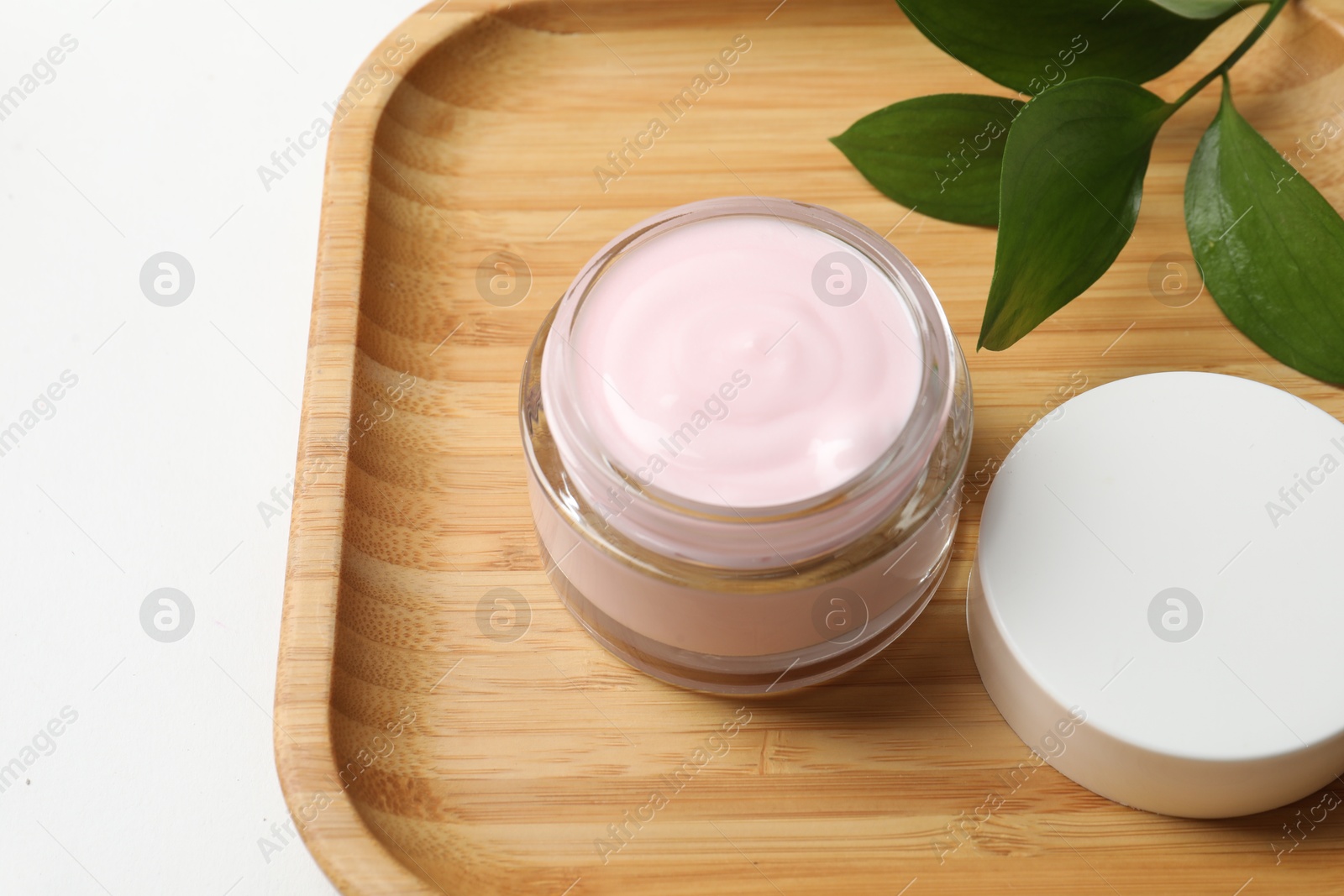 Photo of Jar of cream and green leaves on white table