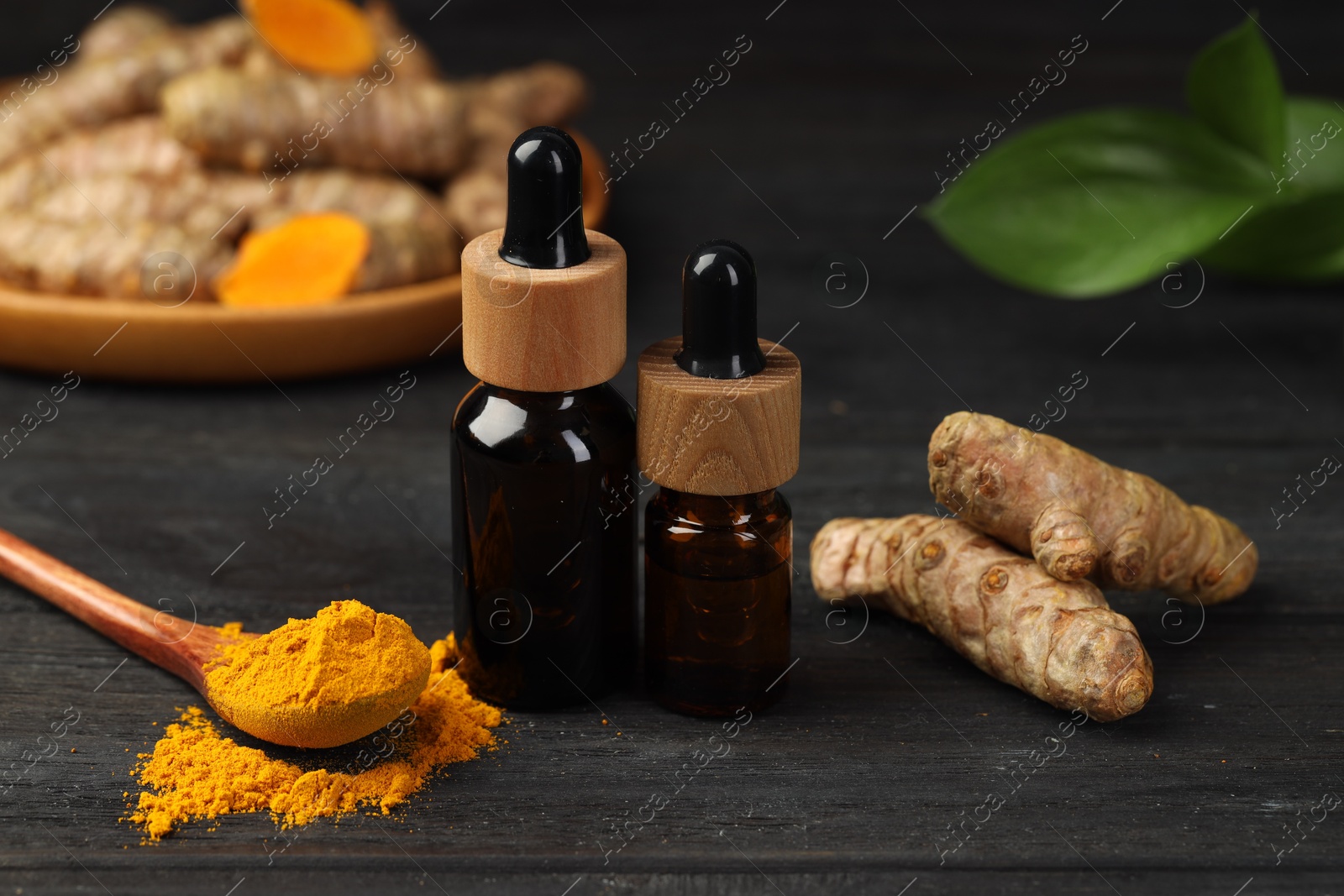 Photo of Turmeric oil, powder, roots and green leaves on dark wooden table, closeup