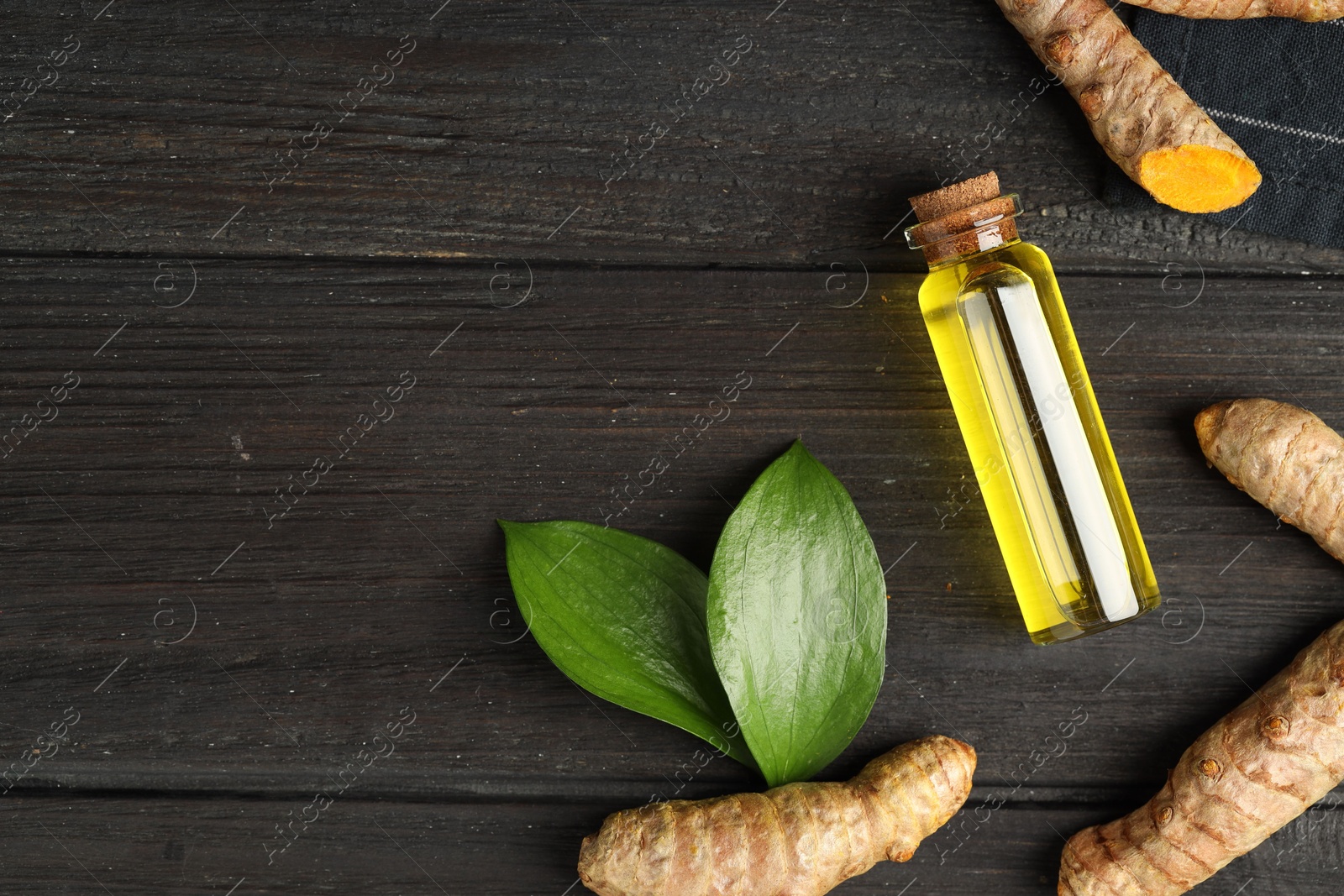 Photo of Turmeric oil, roots and green leaves on dark wooden table, flat lay. Space for text