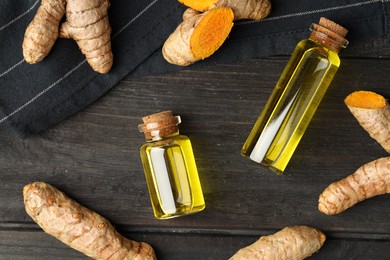 Photo of Turmeric oil and roots on dark wooden table, flat lay