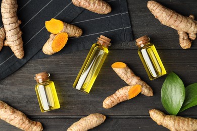 Photo of Turmeric oil, roots and green leaves on dark wooden table, flat lay