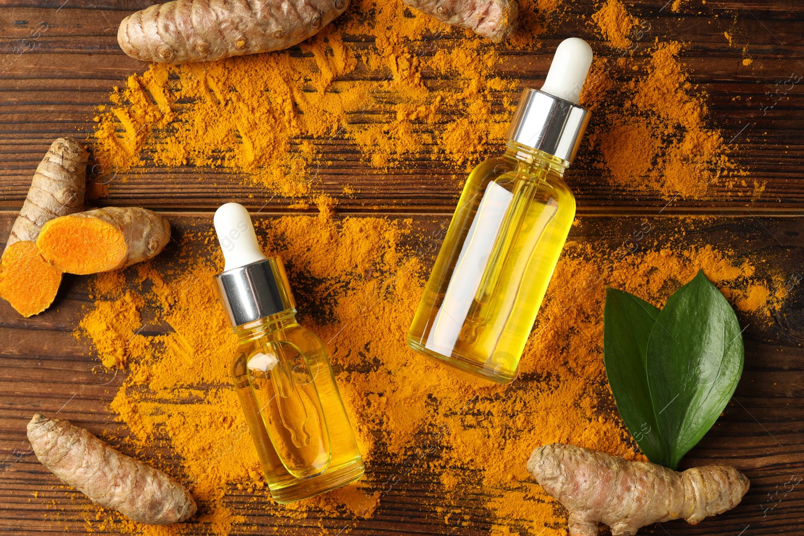 Photo of Turmeric oil, roots and green leaves on wooden table, flat lay