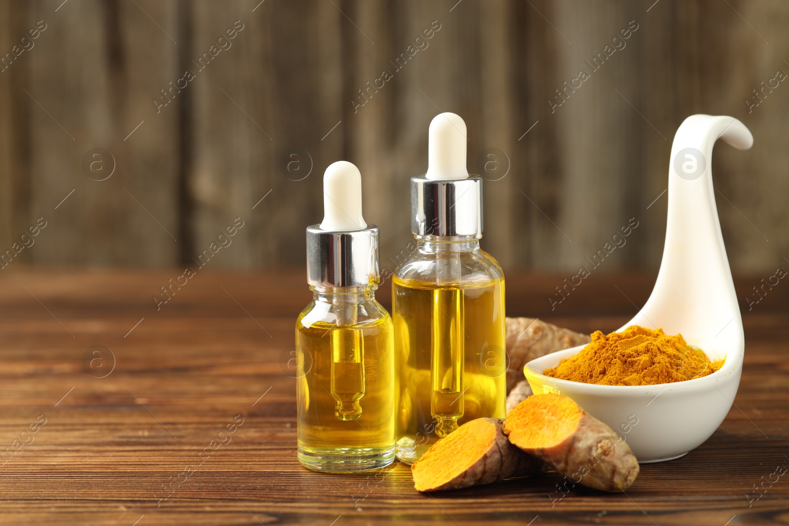 Photo of Turmeric oil, roots and powder on wooden table, space for text