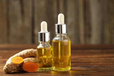 Photo of Turmeric oil and roots on wooden table, closeup. Space for text