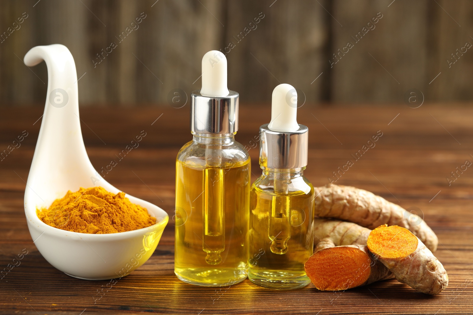 Photo of Turmeric oil, roots and powder on wooden table, closeup