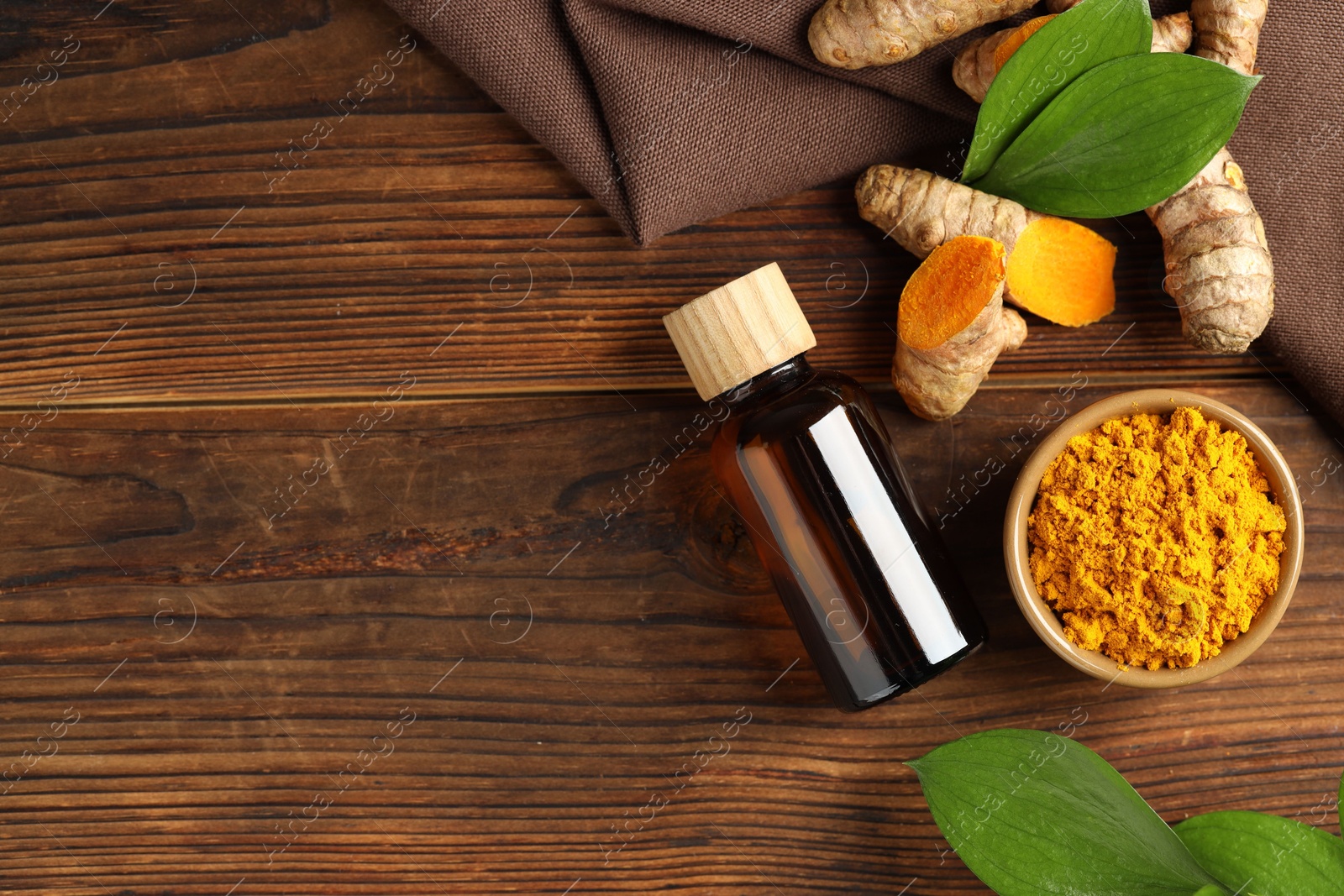 Photo of Turmeric oil, roots, powder and green leaves on wooden table, flat lay. Space for text