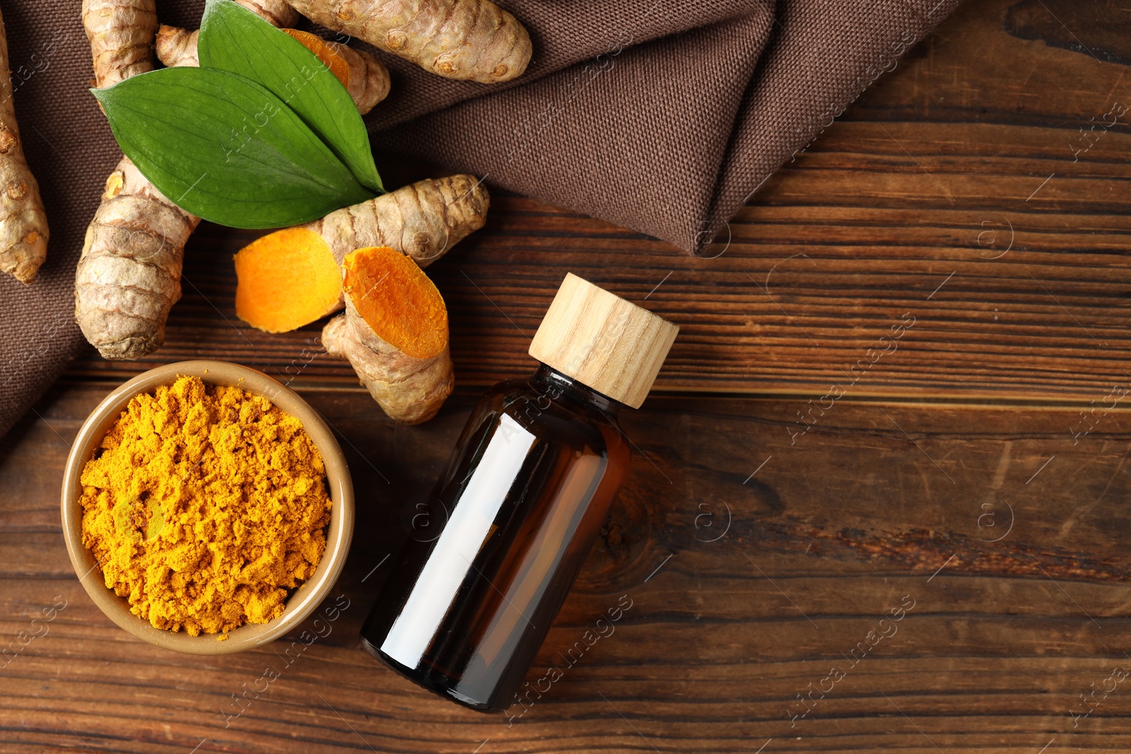 Photo of Turmeric oil, roots, powder and green leaves on wooden table, flat lay. Space for text