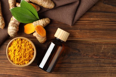 Photo of Turmeric oil, roots, powder and green leaves on wooden table, flat lay. Space for text