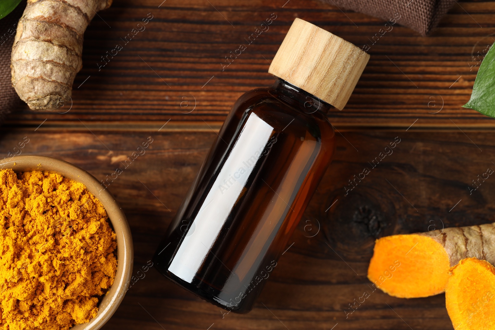 Photo of Turmeric oil, roots and powder on wooden table, flat lay