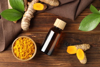 Photo of Turmeric oil, roots, powder and green leaves on wooden table, flat lay