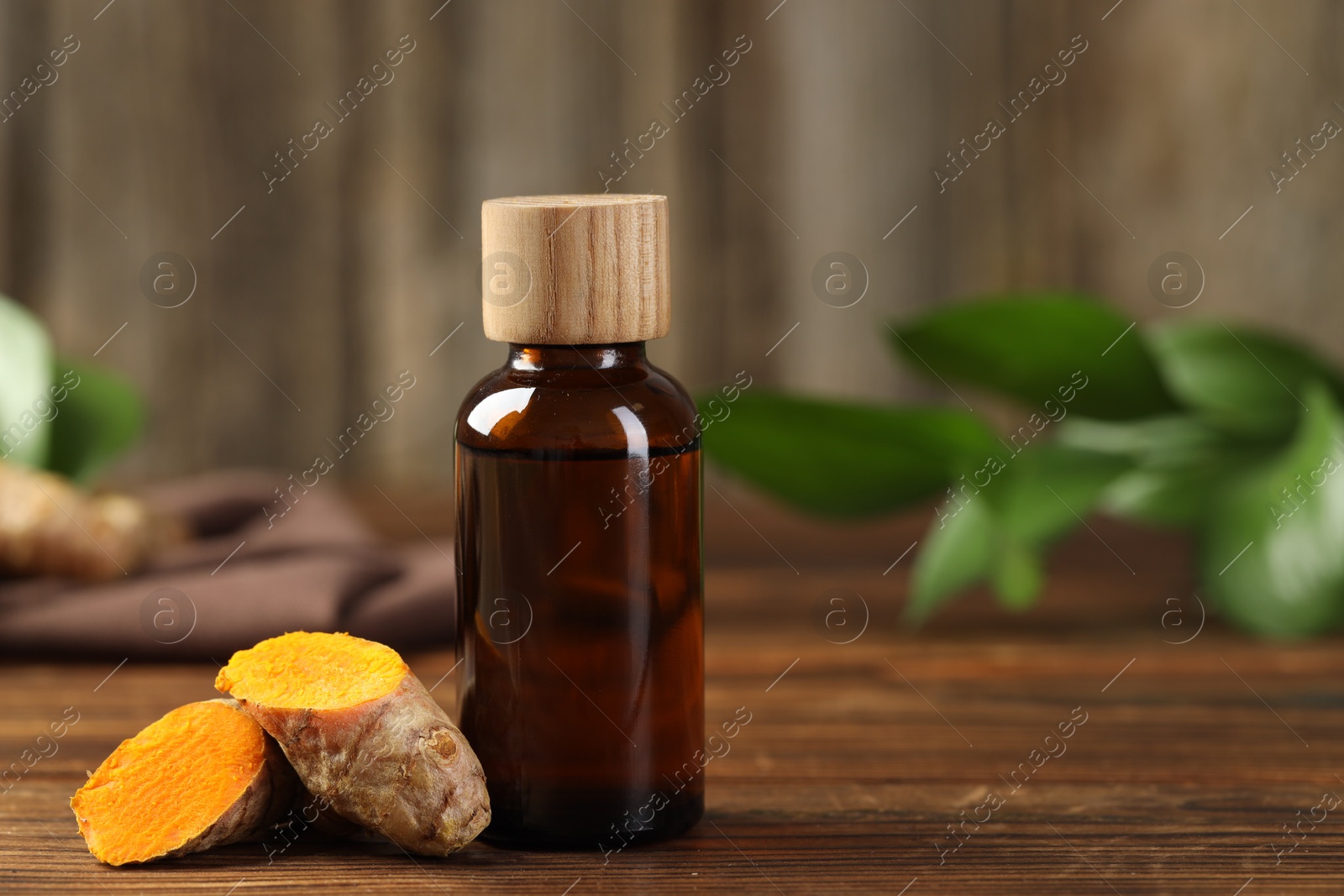 Photo of Turmeric oil and roots on wooden table, closeup. Space for text