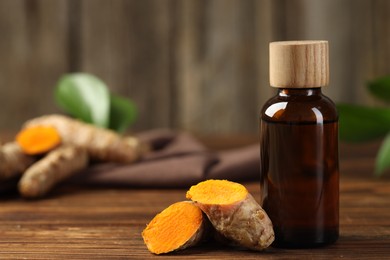 Photo of Turmeric oil and roots on wooden table, closeup. Space for text