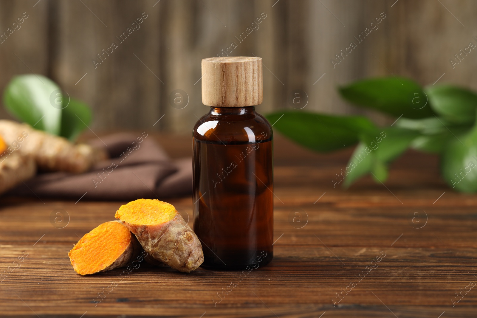 Photo of Turmeric oil and roots on wooden table, space for text