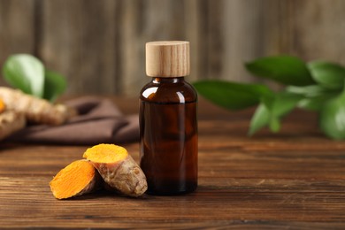 Photo of Turmeric oil and roots on wooden table, space for text